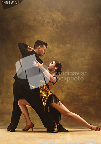 Image of Dance ballroom couple in gold dress dancing on studio background.