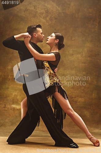 Image of Dance ballroom couple in gold dress dancing on studio background.