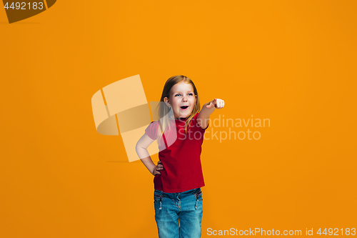 Image of The happy teen girl pointing to you, half length closeup portrait on orange background.