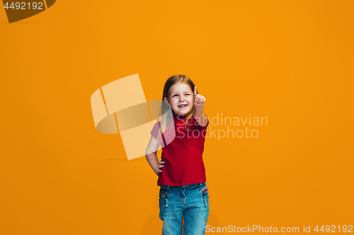 Image of The happy teen girl pointing to you, half length closeup portrait on orange background.