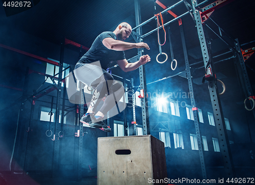 Image of Man jumping during exercises in the fitness gym. CrossFit.