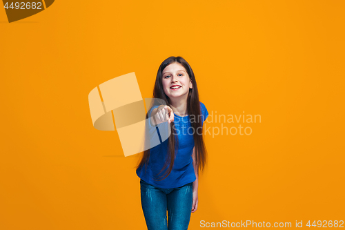 Image of The happy teen girl pointing to you, half length closeup portrait on orange background.