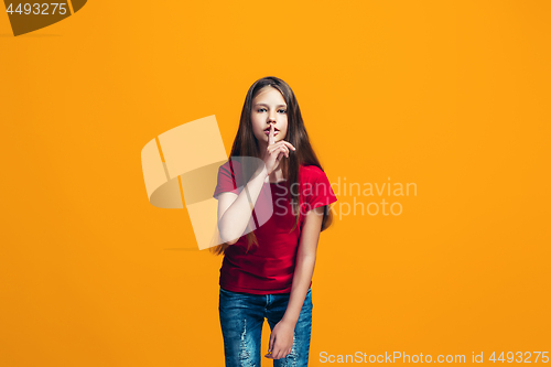 Image of The young teen girl whispering a secret behind her hand over orange background