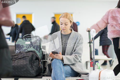 Image of Female traveler using her cell phone while waiting to board a plane at departure gates at airport terminal.