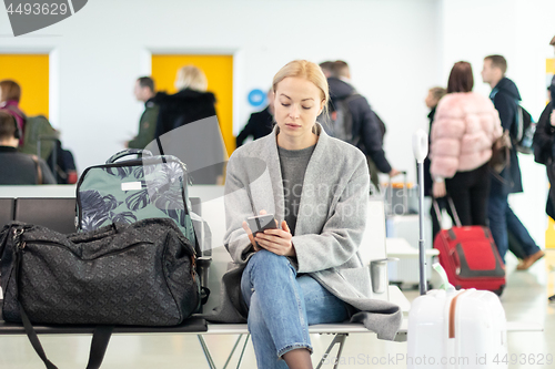 Image of Female traveler using her cell phone while waiting to board a plane at departure gates at airport terminal.