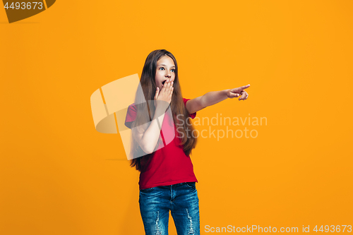 Image of The happy teen girl pointing to you, half length closeup portrait on orange background.