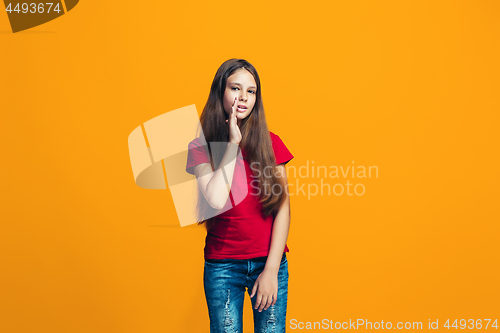 Image of The young teen girl whispering a secret behind her hand over orange background