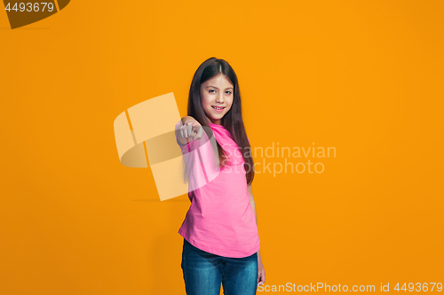 Image of The happy teen girl pointing to you, half length closeup portrait on orange background.