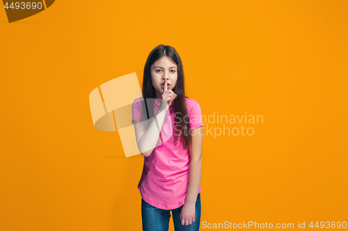 Image of The young teen girl whispering a secret behind her hand over orange background