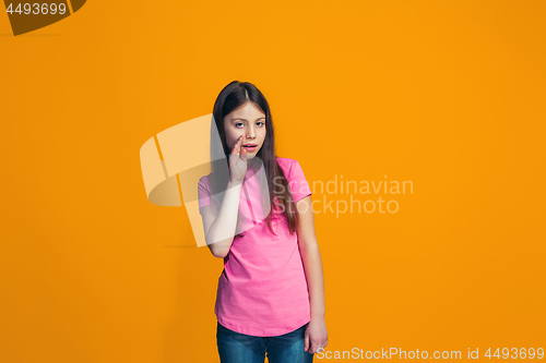 Image of The young teen girl whispering a secret behind her hand over orange background