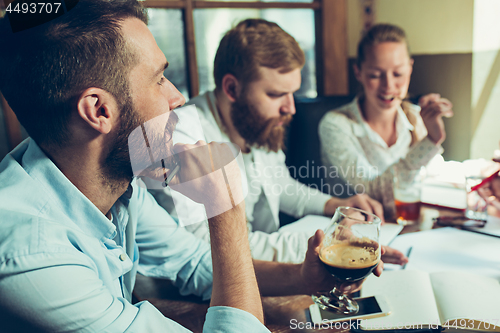 Image of Young cheerful people smile and gesture while relaxing in pub.