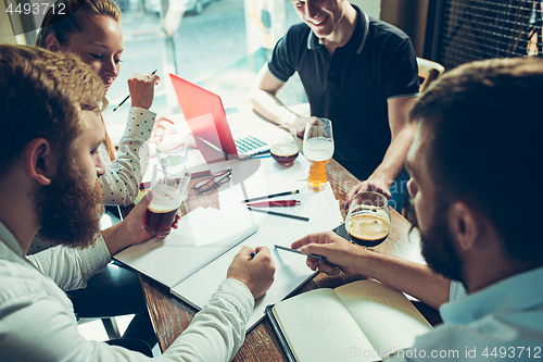 Image of Young cheerful people smile and gesture while relaxing in pub.