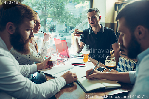 Image of Young cheerful people smile and gesture while relaxing in pub.