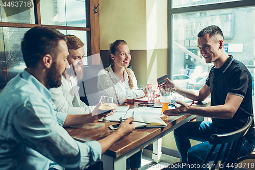 Image of Young cheerful people smile and gesture while relaxing in pub.