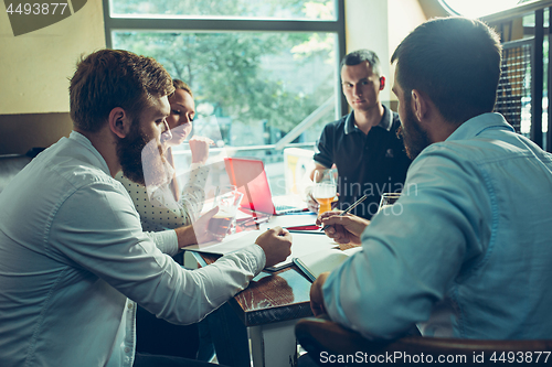 Image of Young cheerful people smile and gesture while relaxing in pub.