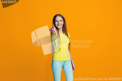 Image of The happy teen girl pointing to you, half length closeup portrait on orange background.