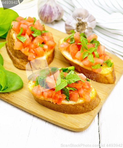 Image of Bruschetta with tomato and spinach on white wooden board