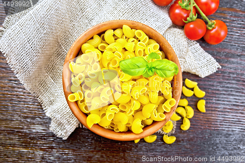 Image of Elbow macaroni in bowl with tomatoes on dark board top