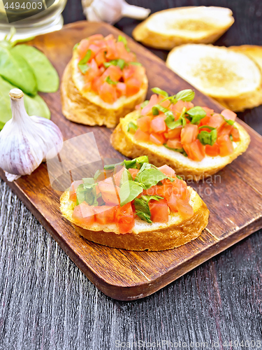 Image of Bruschetta with tomato and spinach on dark wooden board