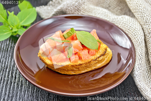 Image of Bruschetta with tomato and basil in brown plate on dark board