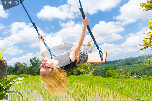 Image of Happy female traveller swinging on wooden swing, enjoying summer vacation among pristine green rice terraces.