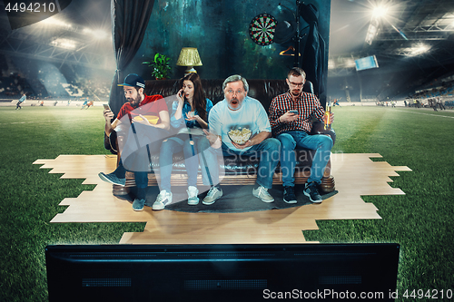 Image of Soccer football fans sitting on the sofa and watching TV in the middle of a football field.