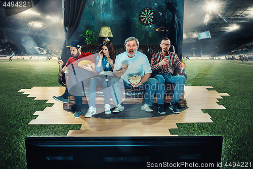 Image of Soccer football fans sitting on the sofa and watching TV in the middle of a football field.