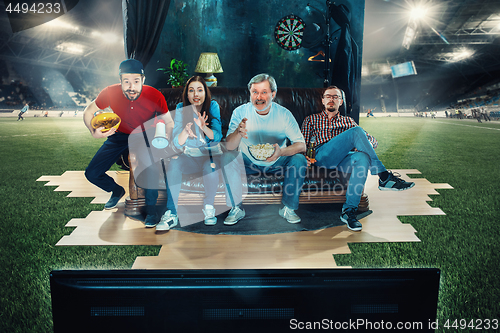 Image of Soccer football fans sitting on the sofa and watching TV in the middle of a football field.