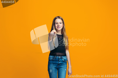 Image of The happy teen girl pointing to you, half length closeup portrait on orange background.