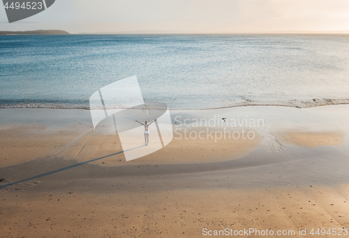 Image of Female stands on a secluded beach at sunset