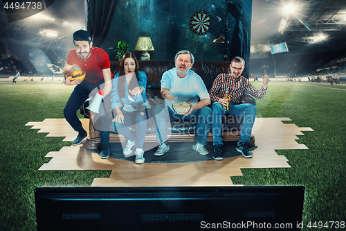 Image of Soccer football fans sitting on the sofa and watching TV in the middle of a football field.