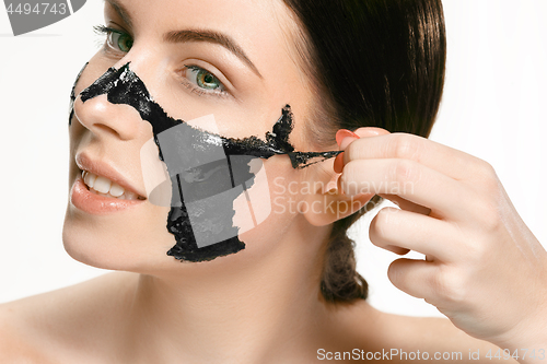 Image of Young beautiful woman applying a mask for the face of the therapeutic black mud. Spa treatment