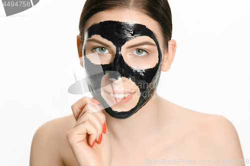 Image of Young beautiful woman applying a mask for the face of the therapeutic black mud. Spa treatment