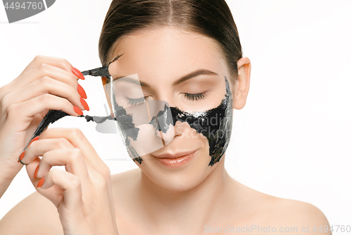 Image of Young beautiful woman applying a mask for the face of the therapeutic black mud. Spa treatment