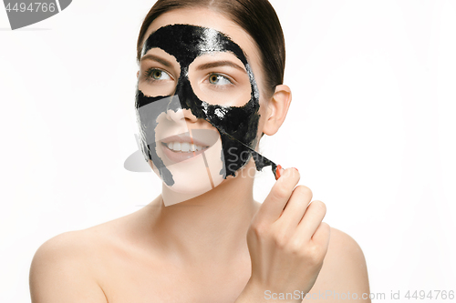 Image of Young beautiful woman applying a mask for the face of the therapeutic black mud. Spa treatment