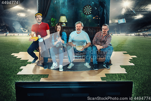 Image of Soccer football fans sitting on the sofa and watching TV in the middle of a football field.