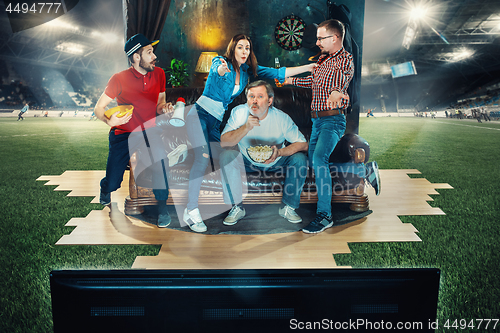 Image of Soccer football fans sitting on the sofa and watching TV in the middle of a football field.