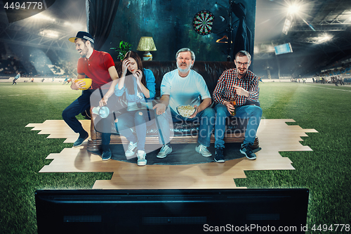 Image of Soccer football fans sitting on the sofa and watching TV in the middle of a football field.