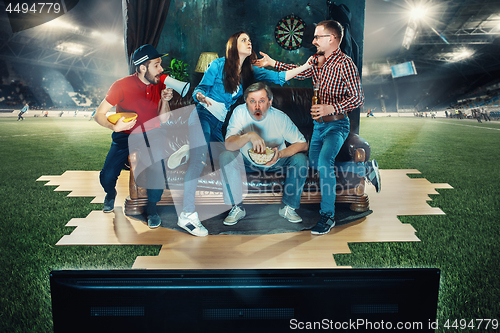 Image of Soccer football fans sitting on the sofa and watching TV in the middle of a football field.