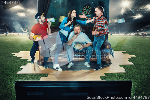 Image of Soccer football fans sitting on the sofa and watching TV in the middle of a football field.