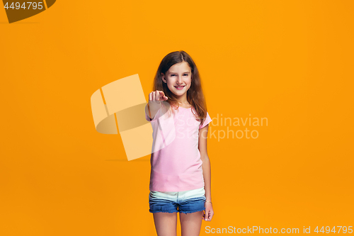 Image of The happy teen girl pointing to you, half length closeup portrait on orange background.