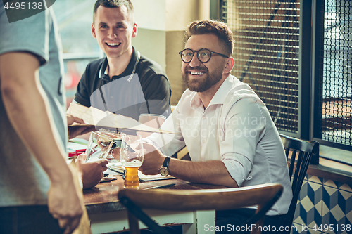 Image of Young cheerful people smile and gesture while relaxing in pub.