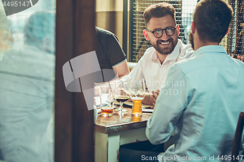 Image of Young cheerful people smile and gesture while relaxing in pub.