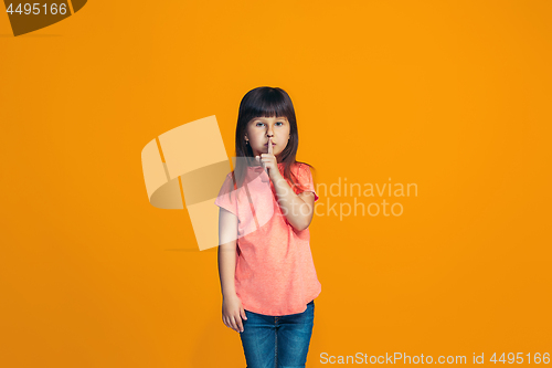 Image of The young teen girl whispering a secret behind her hand over orange background