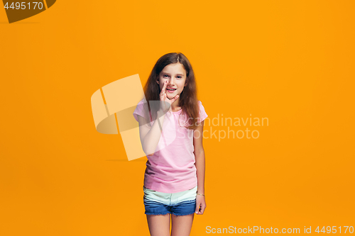 Image of The young teen girl whispering a secret behind her hand over orange background