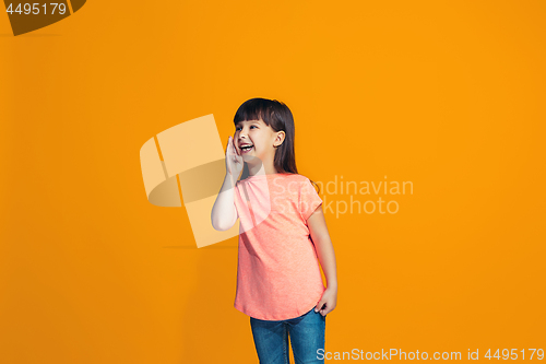 Image of The young teen girl whispering a secret behind her hand over orange background
