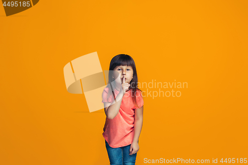 Image of The young teen girl whispering a secret behind her hand over orange background