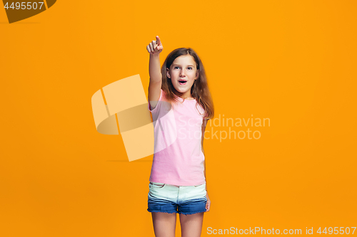 Image of The happy teen girl pointing to you, half length closeup portrait on orange background.