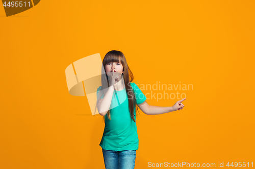 Image of The young teen girl whispering a secret behind her hand over orange background