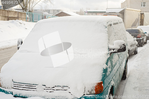 Image of Green car is covered with snow parked near the street.